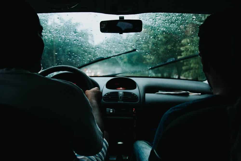 Windshield wipers are seen on a windshield from inside a car driving through rain.