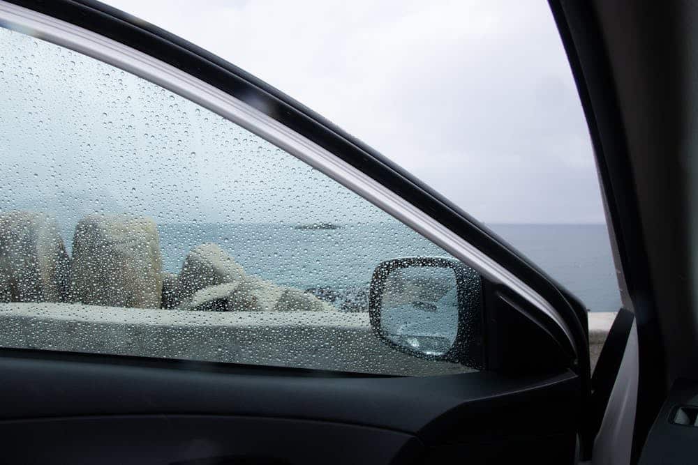 pexels-dorota-semla-1929451-8969239 A car interior view on a rainy day, showing raindrops on the side window overlooking a rocky coastline and gray waters outside.